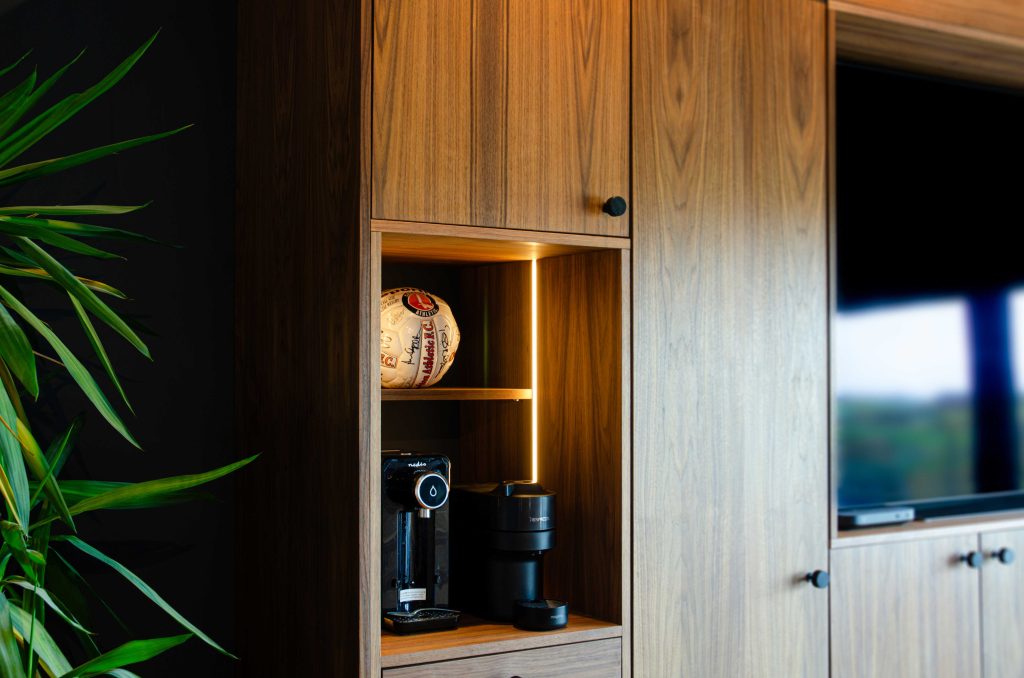 A walnut coloured storage solution with built-in TV screen and section for coffee making and displaying a signed football.